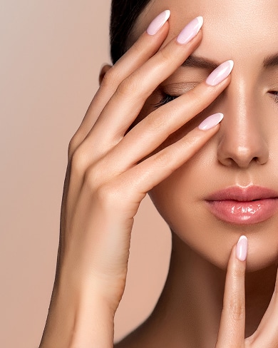 Manucure French Pâle : Ongles Élégants & Peau Lumineuse Gros plan sur le visage d'une femme avec manucure french manucure rose pâle et doigts touchant délicatement le visage.