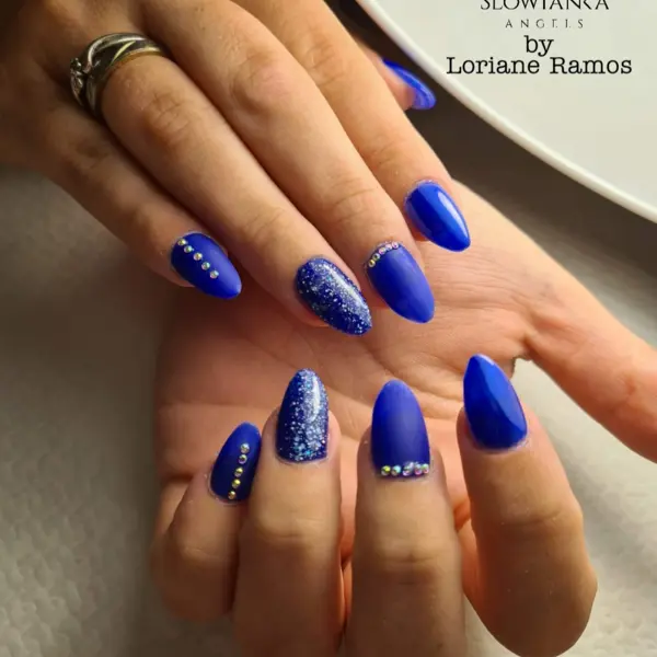 Mains ornées d'une manucure bleu roi mat et pailleté, décorée de strass. Texte visible : SLOWIANKA ANGELIS by Loriane Ramos.