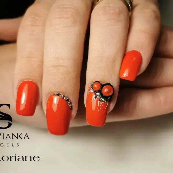 Manucure ongles carrés courts rouge corail avec strass noirs et décorations 3D rouges texturées, visiblement la marque SWIANKA GELs Loriane.